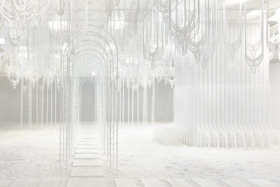 an all-white installation of intricate metalwork in a white exhibition space