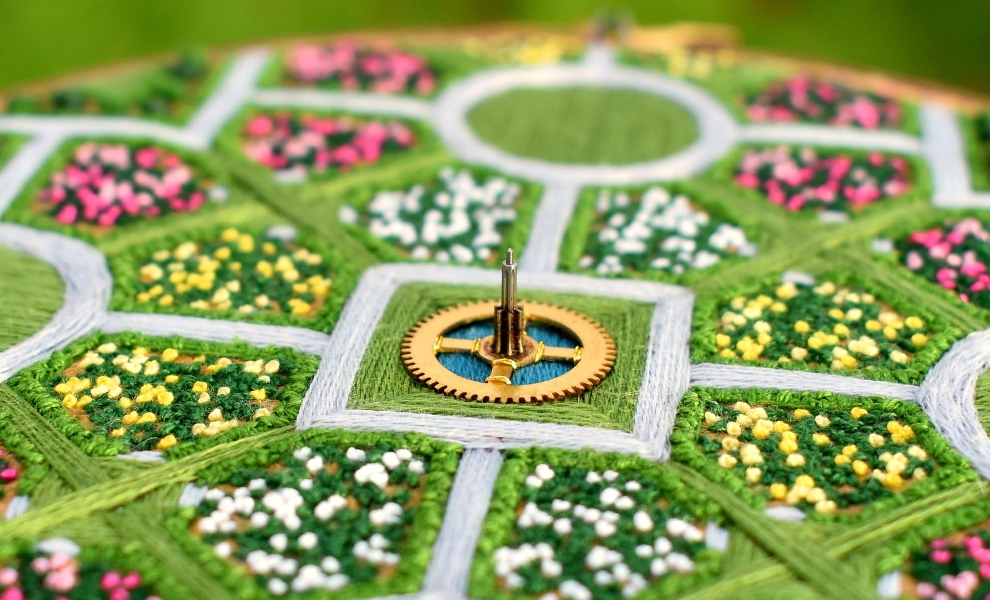 detail of a lush aerial landscape of a symmetrical garden with flowers and walkways stitched with thread inside an embroidery hoop