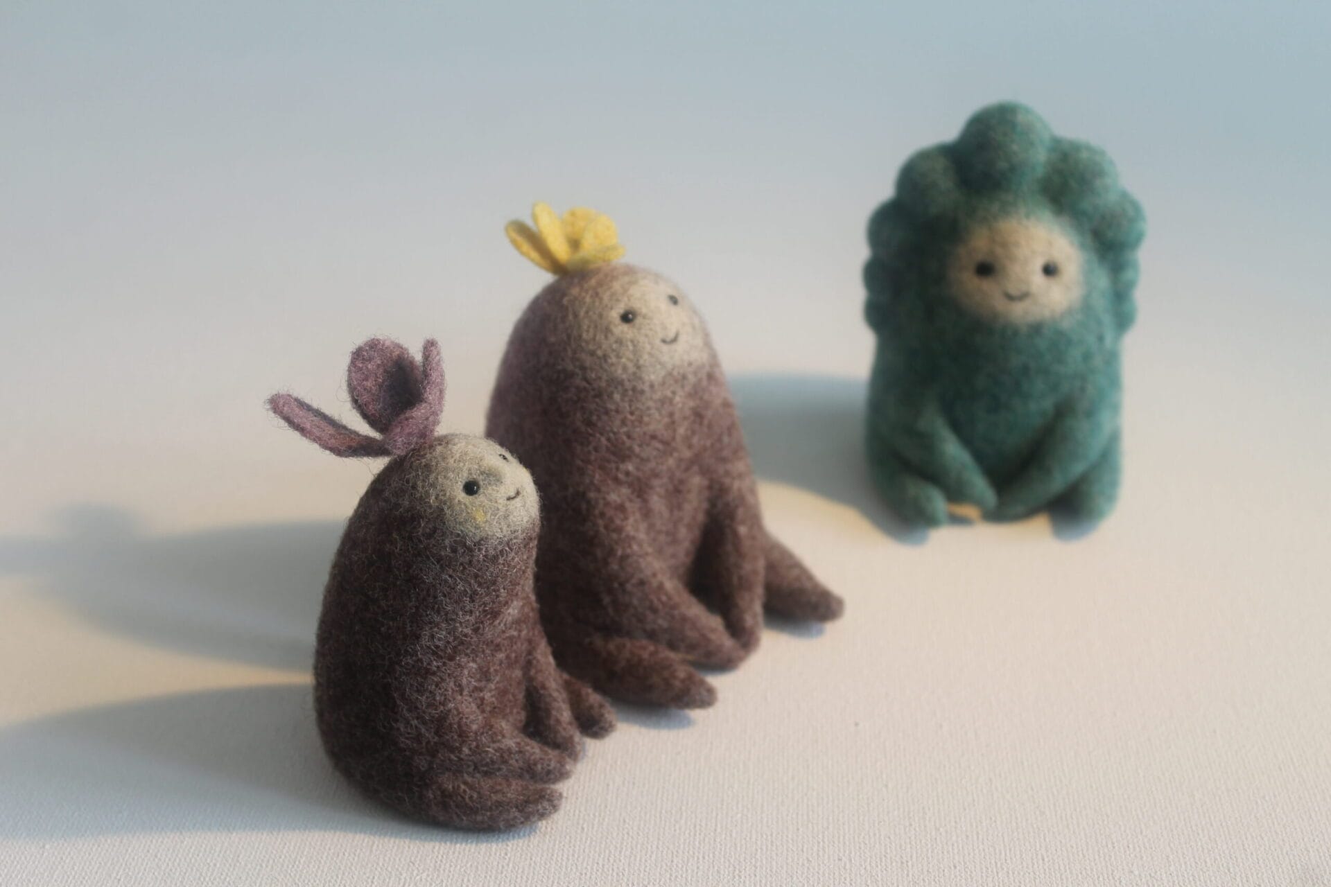 three small, felted creatures donning sprouts on their heads sit together