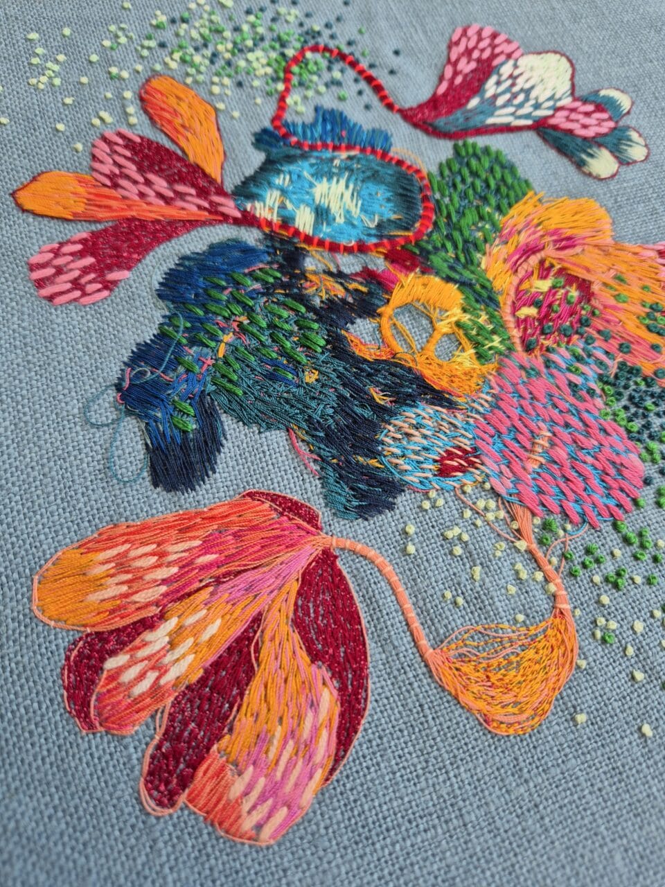 a detail of a colorful abstract embroidery on blue fabric