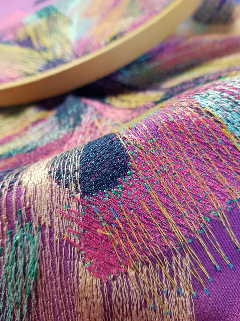 a detail of a colorful abstract embroidery on pink fabric