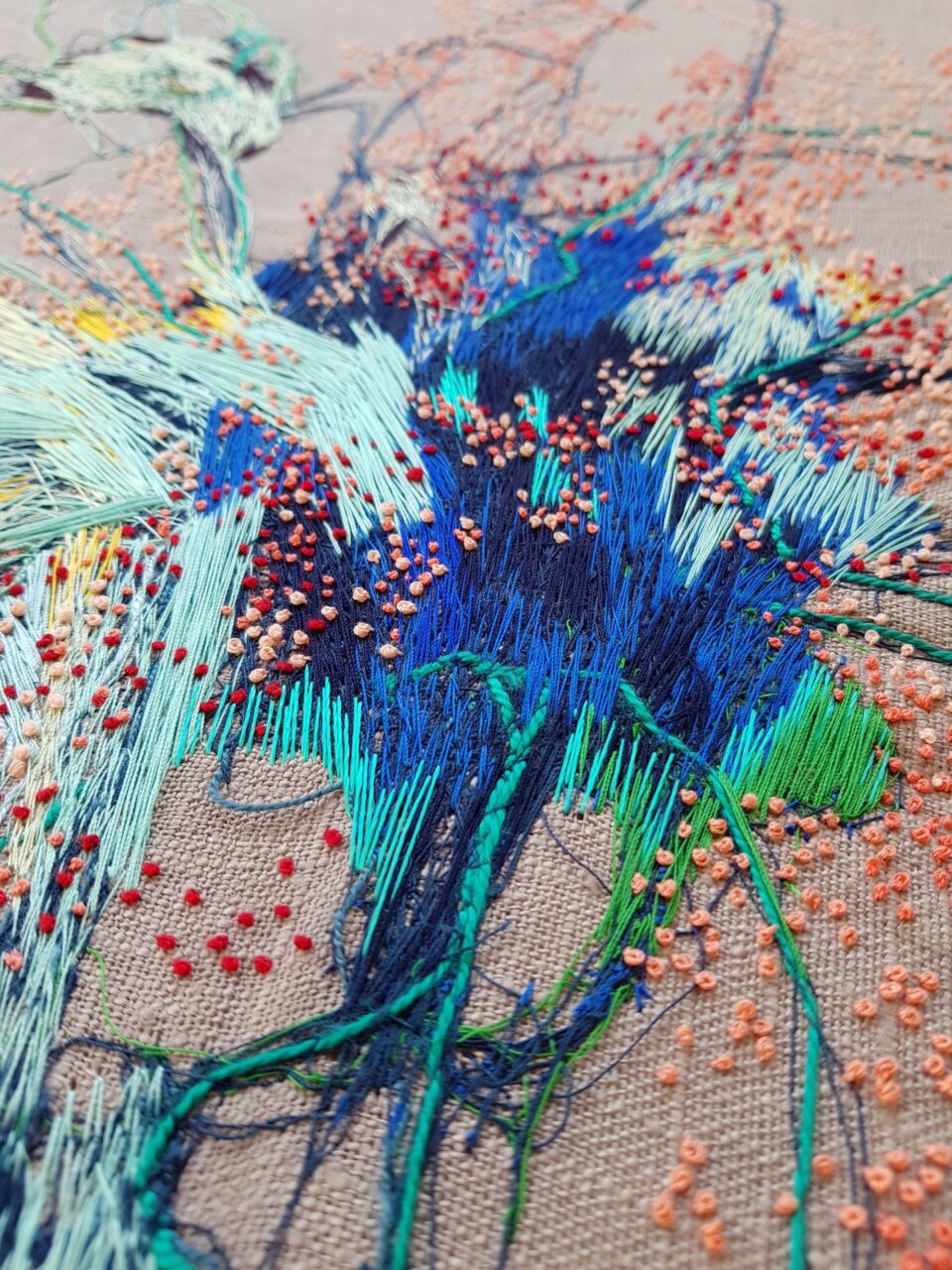 a detail of a colorful abstract embroidery on tan fabric