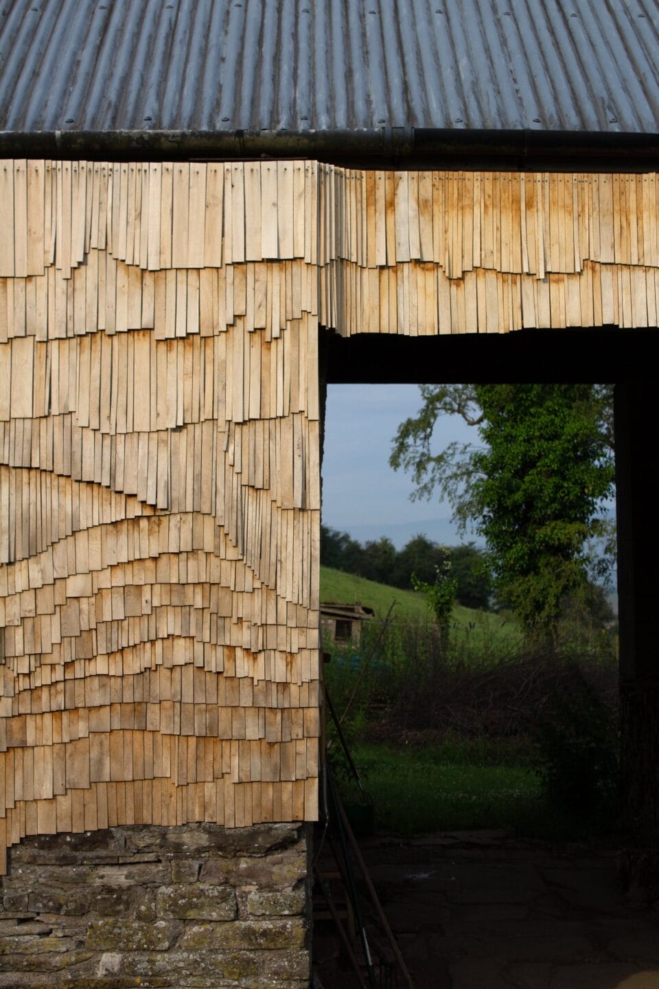 detail of the side of an old stone barn clad in tiny wooden shingles in an undulating pattern