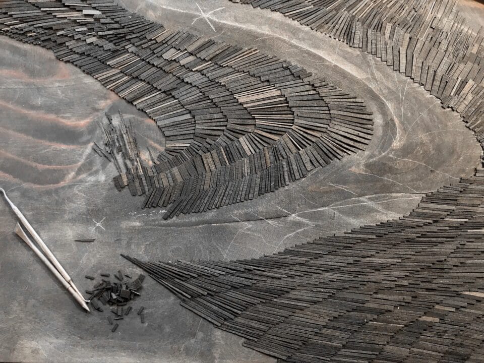 an artwork in progress made of hundreds of tiny wooden shingles in curved arrangements