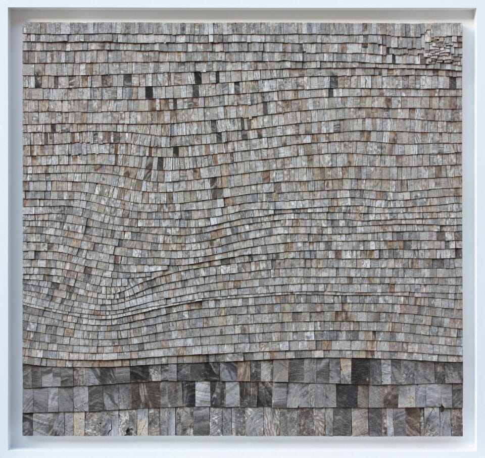 an abstract artwork in a long, horizontal format, made from tiny, gray wooden shingles