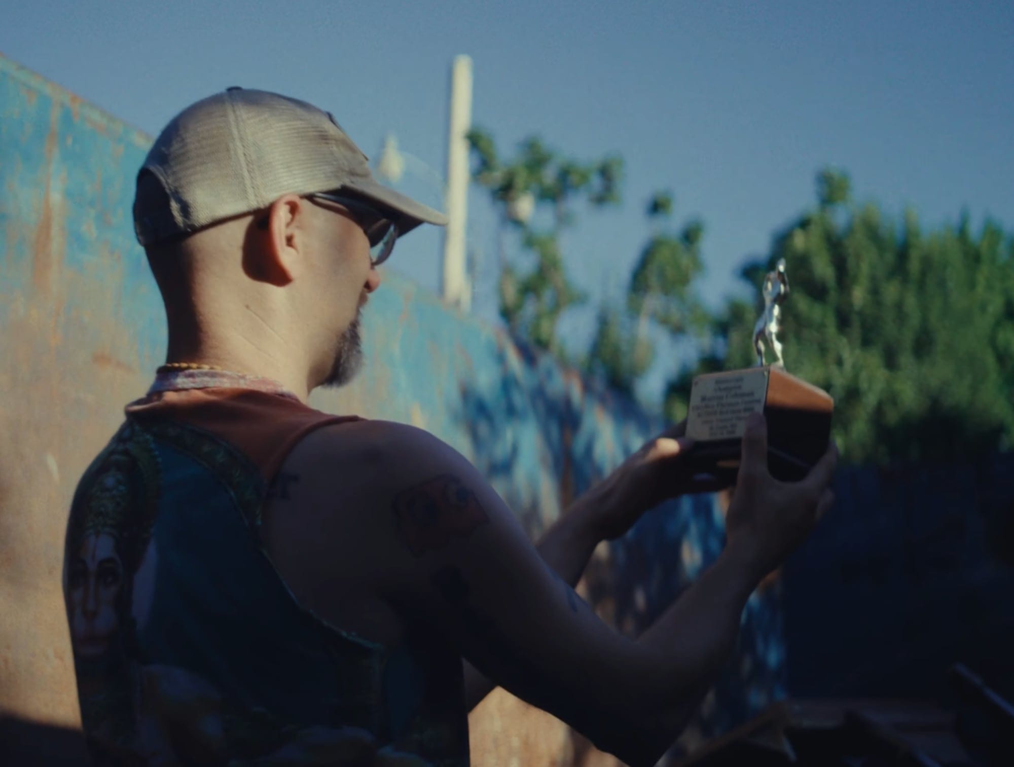 a white man in a hat holds up a trophy while standing in a dumpster