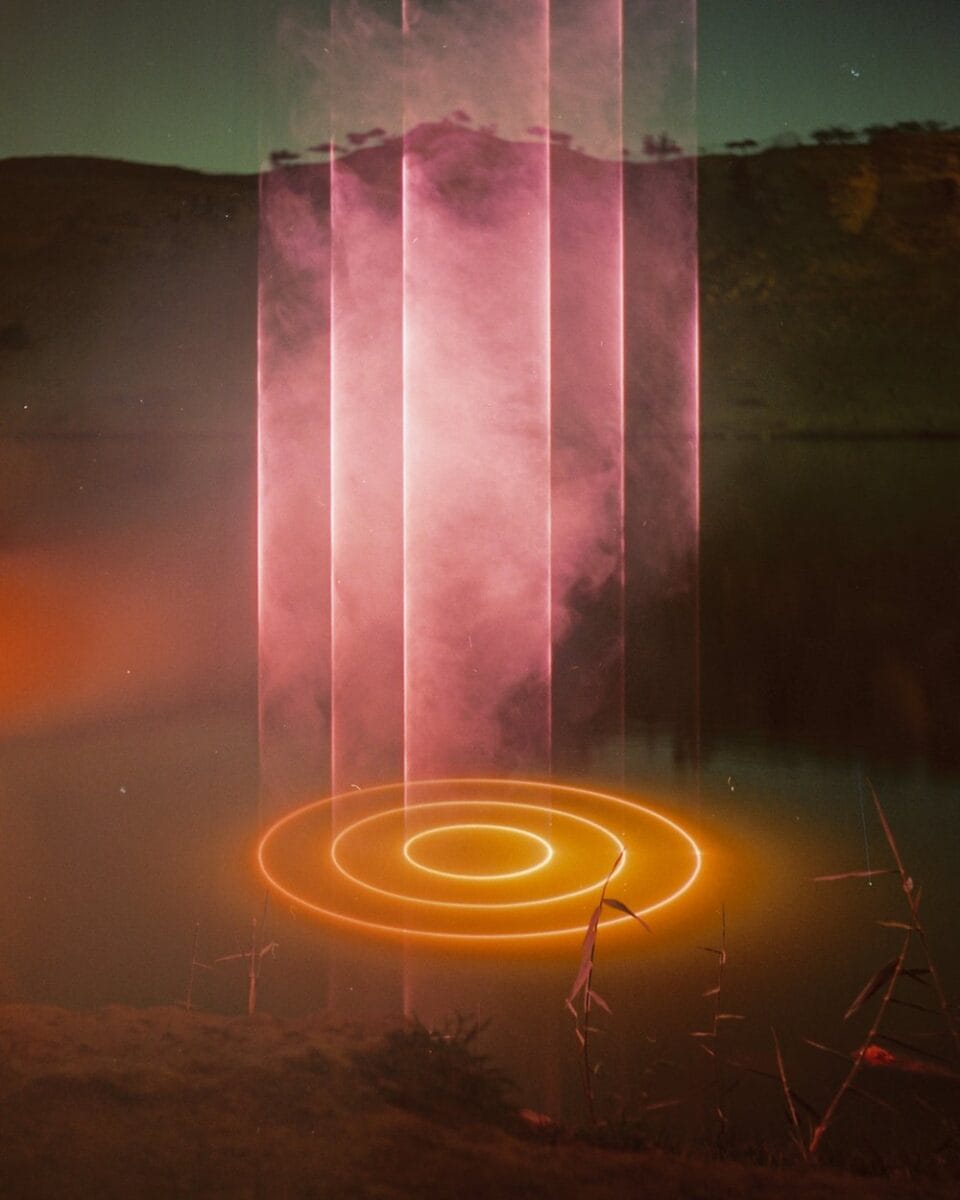 a photograph of a light projection on a body of water, creating three concentric circles in orange on the surface of the water, with misty air interacting with the beams above the shape