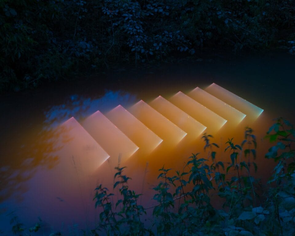 a dark body of water with a peach-colored geometric light projection in the surface of the water