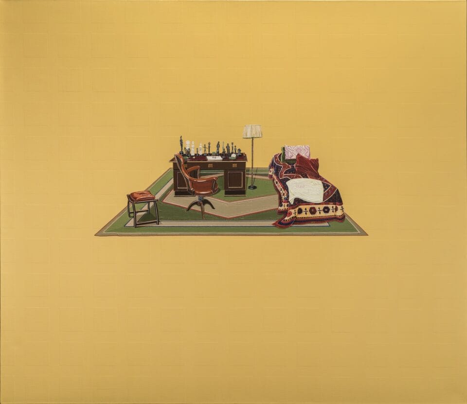 In the middle of a mustard yellow canvas is a small painting of a wooden desk and brown chair. On the desk are various small figurines. A floor lamp and small bed are to the right. The bed is covered with pillows and an ornately designed comforter.